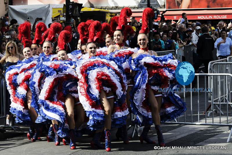 Moulin Rouge dancers walk toward the performance area before the final stage of the 2026 Tour de France in Paris.