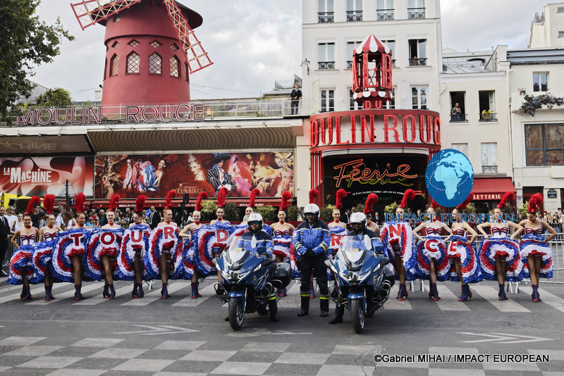 French police motorcycle officers pose in front of Moulin Rouge dancers before the final stage of the 2026 Tour de France in Paris.