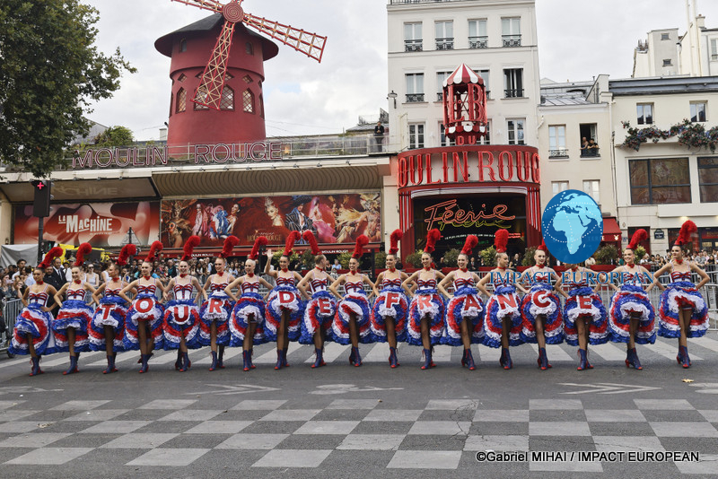 A Tour de France rider passes in front of Moulin Rouge dancers performing outside the famous Paris cabaret.