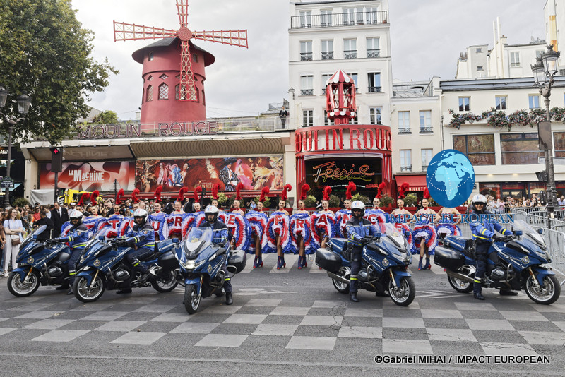 French police motorcycle officers pose in front of Moulin Rouge dancers before the final stage of the 2026 Tour de France in Paris.