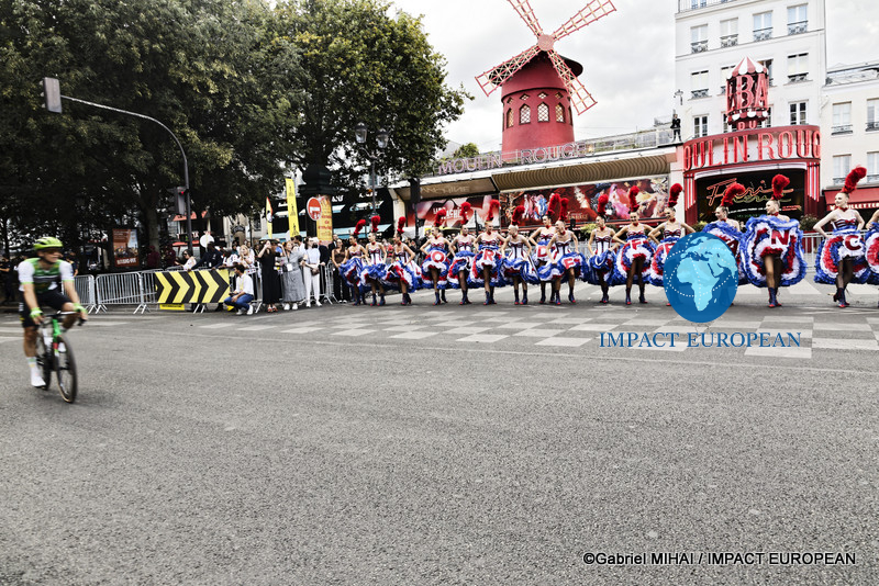 Several Tour de France riders pass the Moulin Rouge as dancers continue their performance in Paris.